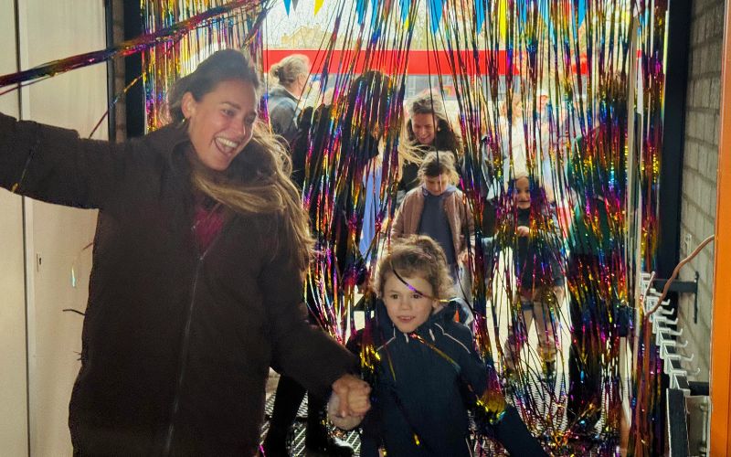 Tijdens de feestelijke opening lopen de leerkracht en een leerling van de nieuwe Samen naar School‑klas van Stichting KIO symbolisch door de glitterwand.