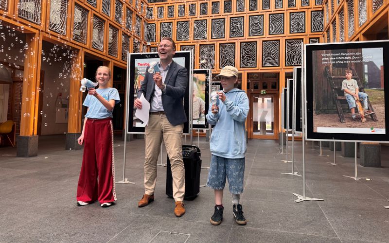 Met een bellenblaaspistool opent wethouder Lars Wijnhoud samen met Sophie en Benjamin  de tentoonstelling: ‘Samen Opgroeien. Gewoon in Deventer.’