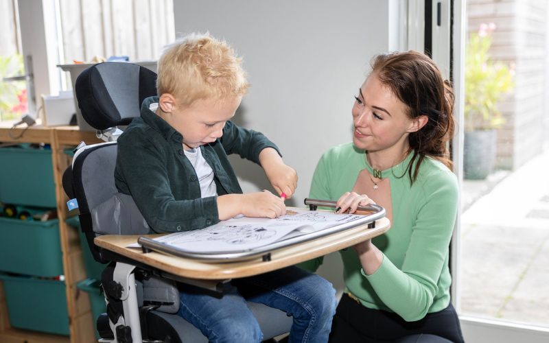 Jayce in zijn stoel aan het kleuren, moeder Nadine ernaast