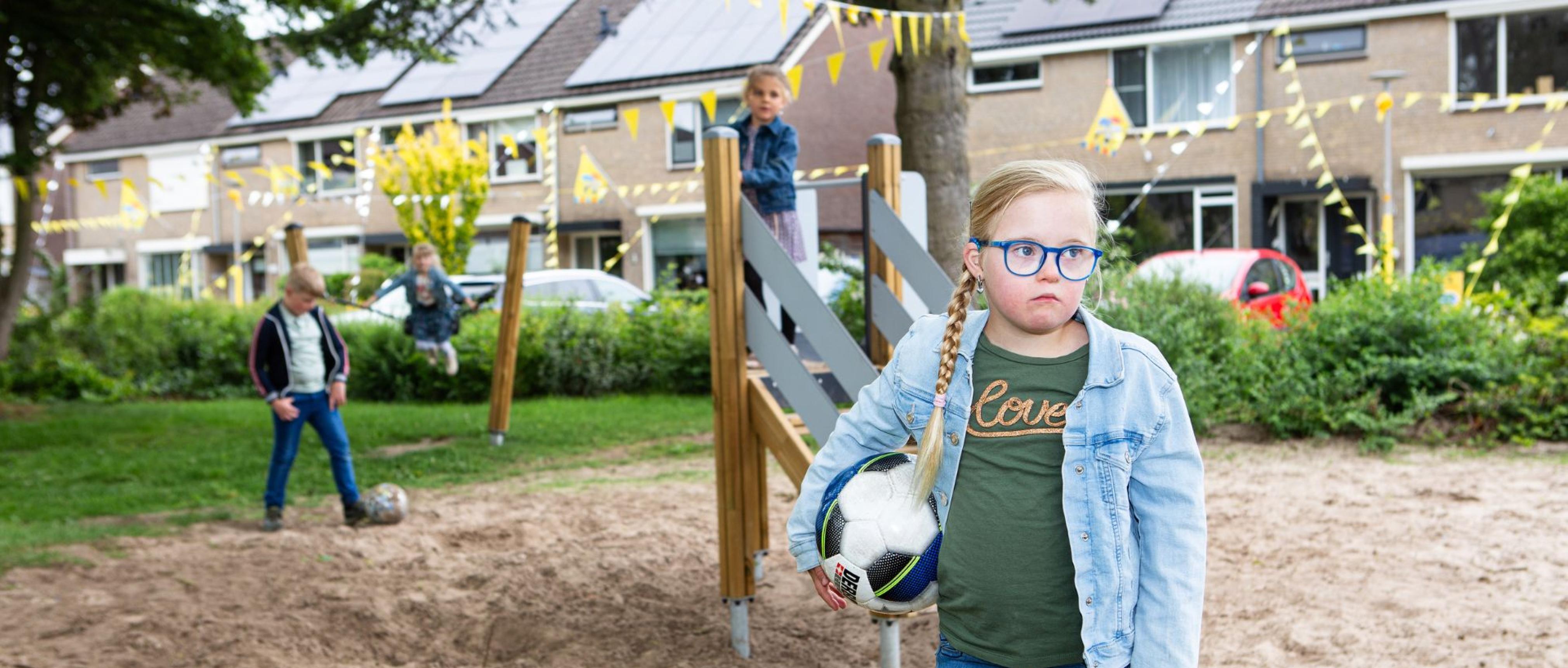 meisje met voetbal onder arm op speelplek, ze kijkt somber