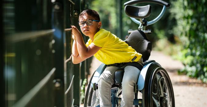 Jayden in zijn rolstoel voor een hek