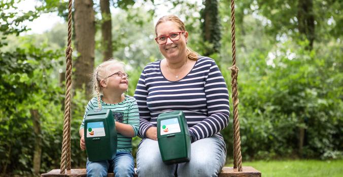 Lotte en haar moeder Linda op een schommel met een collectebus in hun handen