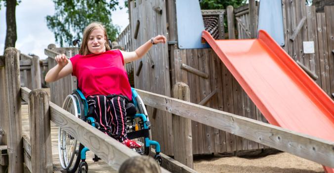 Luna die van een rolstoeltoegankelijke glijbaan afgaat met haar rolstoel op een samenspeelplek
