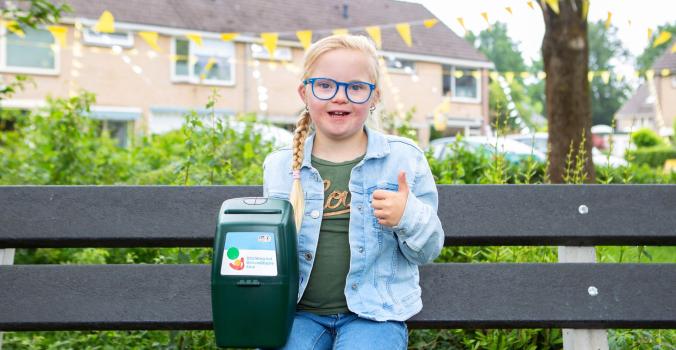 Lotte op een bankje met een collectebus en duim ophoog