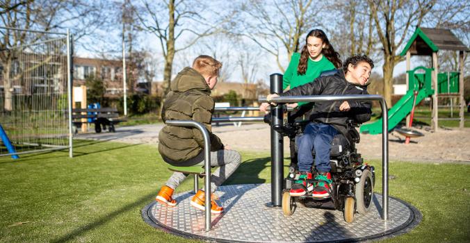 Ira in zijn rolstoel op een toegankelijke draaimolen samen met twee vriendjes