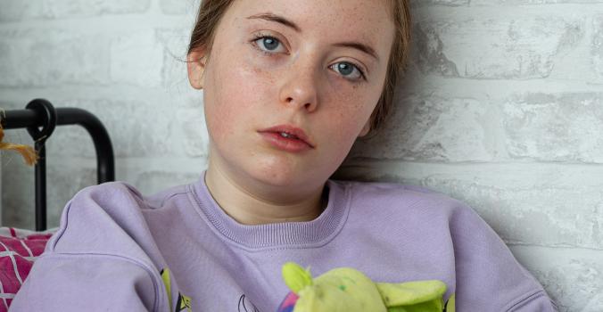 Leona zittend op bed en kijkt je aan