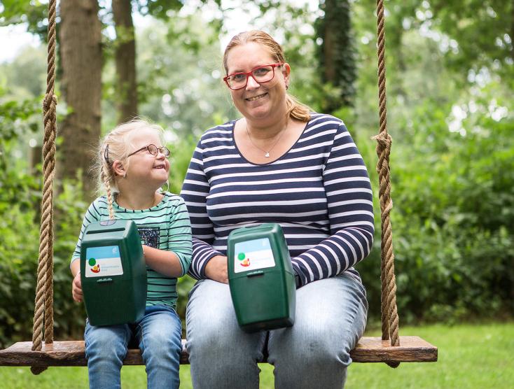 Lotte en haar moeder Linda op een schommel met een collectebus in hun handen