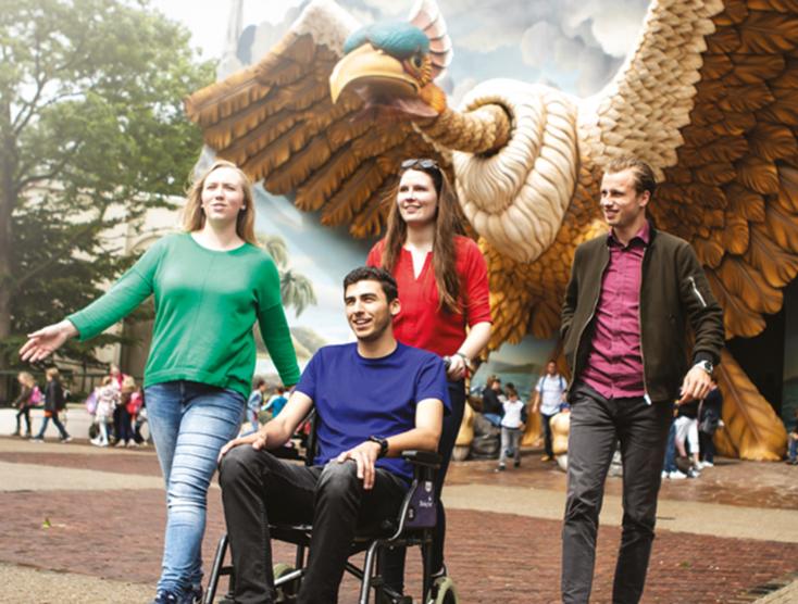 Bezoeker in een rolstoel met gezelschap lopend in de Efteling