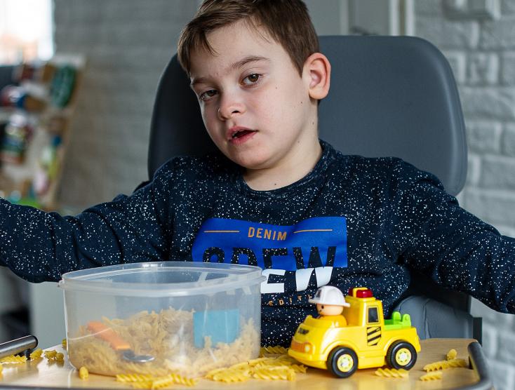 Gideon zit in een stoel met speelgoed te spelen