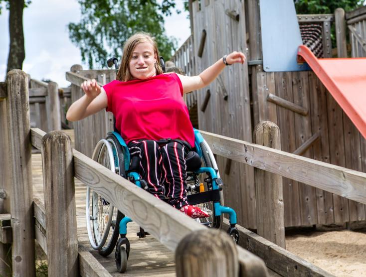 Luna die van een rolstoeltoegankelijke glijbaan afgaat met haar rolstoel op een samenspeelplek