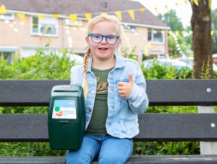 Lotte op een bankje met een collectebus en duim ophoog