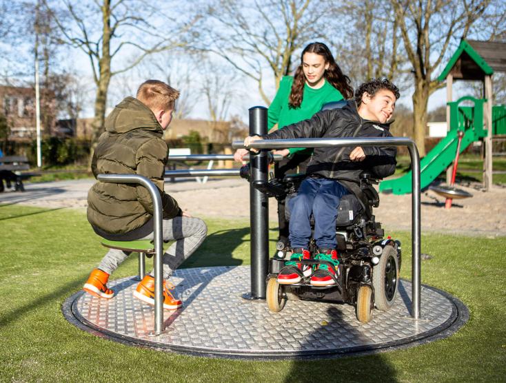 Ira in zijn rolstoel op een toegankelijke draaimolen samen met twee vriendjes