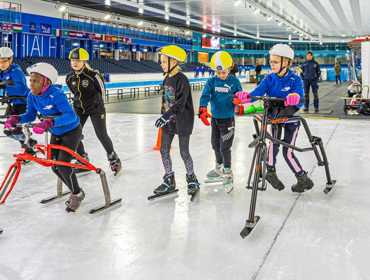 Kinderen met een beperking op een schaatsframe aan het schaatsen en naast hun schaatsen kinderen zonder beperking | Frame Schaatsen