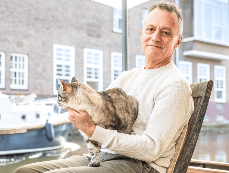 Foto van Ian Helgering met zijn kat Hector op schoot bij een raam.