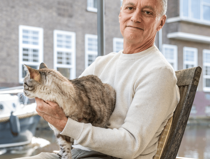 Ian zit met zijn kat op schoot aan tafel in zijn woonboot